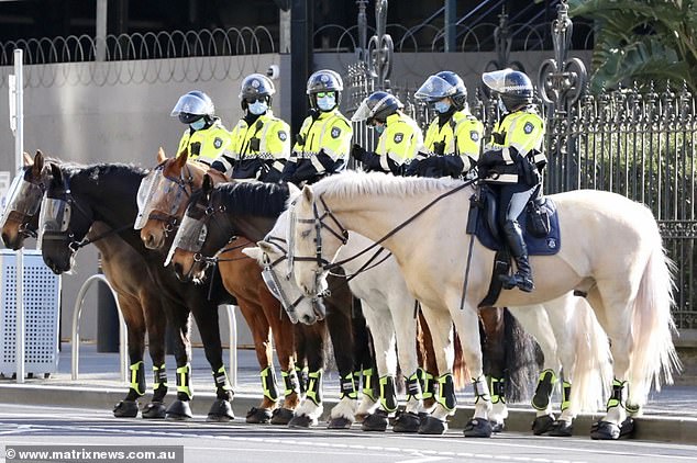 Police line up on horseback in Melbourne as hundreds of protesters descend onto the coronavirus-riddled city on Saturday