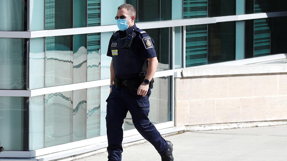 Un agent de l'Agence des services frontaliers du Canada  qui marche, en uniforme, portant un masque et des verres fumés.