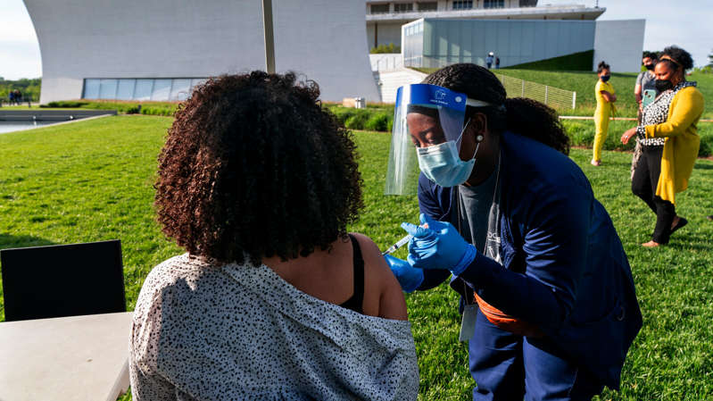 a group of people that are standing in the grass: A woman receiving the J & J vaccine last Thursday at the Kennedy Center in Washington.
