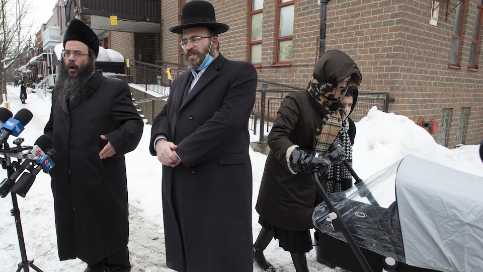 Abraham Ekstein et Max Lieberman du Conseil des juifs hassidiques du Québec s'adressent à des journalistes pendant qu'une mère passe avec ses enfants dans une rue du quartier Outremont, à Montréal.
