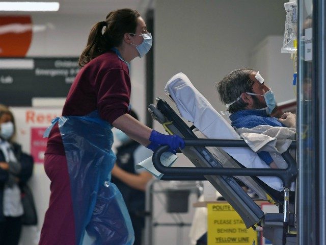 A medical professional in PPE, including gloves, an apron and a face mask as a precautionary measure against Covid-19, pushes a patient, also wearing a facemask, as he lays on a bed, inside St Thomas' Hospital in north London, on April 1, 2020, as life in Britain continues during the …